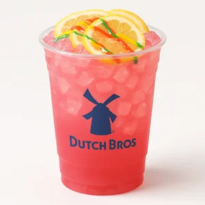 Dutch Bros Starburst Lemonade in a clear cup with ice, pink color, lemon garnish, and candy drizzle.

